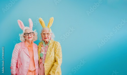 Cute fun older ladies wearing easter bunny ears and celebrate Easter holiday against a blue background.