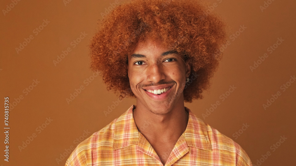 Close up, stylish curly guy looks at the camera with smile isolated on brown background in the studio Close up, stylish curly guy looks at the camera with smile isolated on brown background in the studio