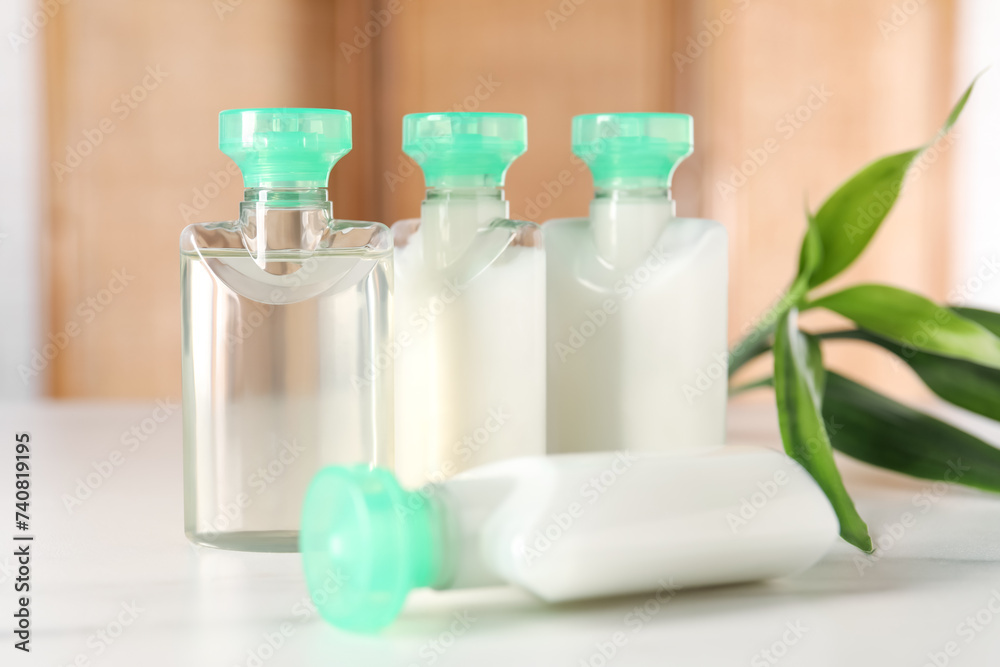Mini bottles of cosmetic products and green branch on white table against blurred background, closeup Mini bottles of cosmetic products and green branch on white table against blurred background, closeup