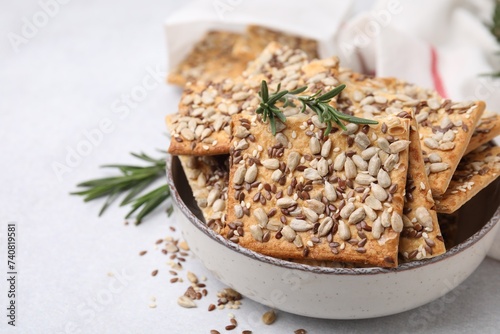 Cereal crackers with flax, sunflower, sesame seeds and rosemary in bowl on light table, closeup. Space for text