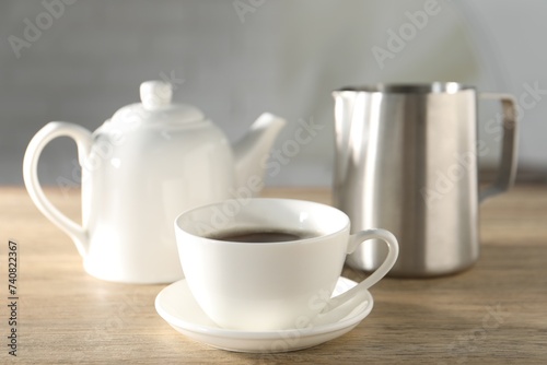 Aromatic tea in cup, teapot and pitcher on wooden table