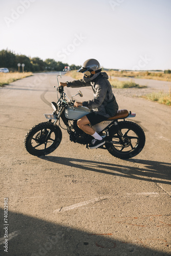 Biker on a cafe racer motorcycle on the road at sunset.