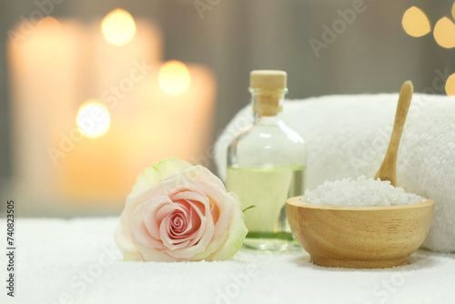 Beautiful spa composition with essential oil, sea salt and rose on white towel against blurred background. Space for text