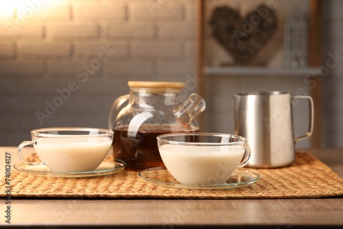 Tasty milk in glass cups, pitcher and teapot with tea on wooden table