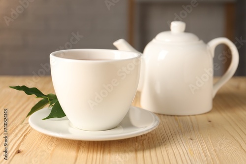 Cup and teapot on light wooden table, closeup