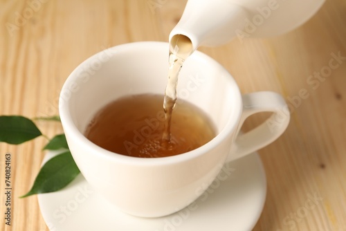 Pouring tasty tea into cup at light wooden table, closeup