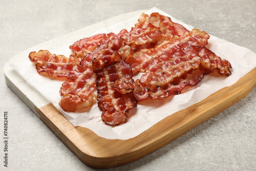 Board with fried bacon slices on grey textured table, closeup Board with fried bacon slices on grey textured table, closeup