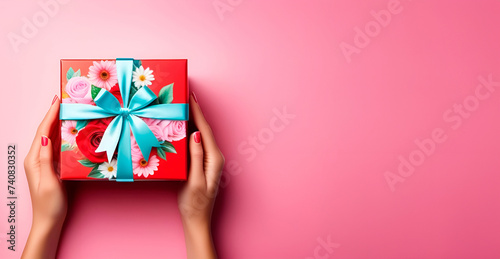 Female hands with gift box decorated with flowers on pink background. Holiday gift. Space for copying, place for text. Layout, template, mockup