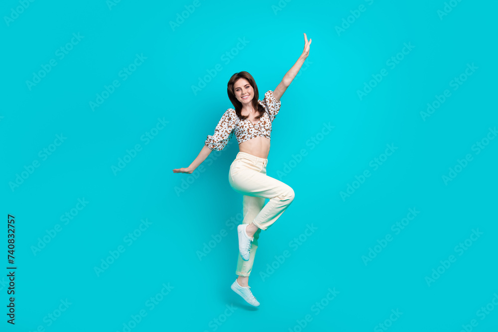 Full length photo of cute impressed woman wear flower print top jumping high arms sides isolated teal color background