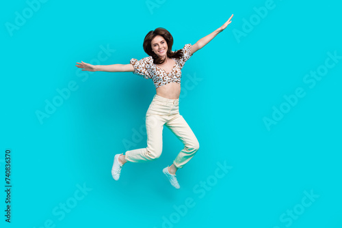 Full length photo of excited pretty lady dressed flower print top arms sides jumping high isolated turquoise color background