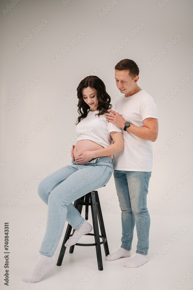 Pregnant woman and handsome man hugging tummy at home. Pregnant family isolated on white studio background. Husband embraces belly wife. Nine months. Loving couple smiling embrace together. Pregnant woman and handsome man hugging tummy at home. Pregnant family isolated on white studio background. Husband embraces belly wife. Nine months. Loving couple smiling embrace together.
