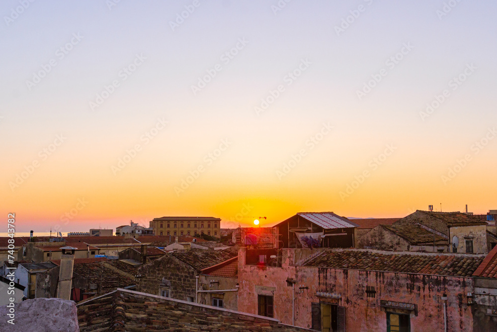 View of the rising sun above the rooftops against the pink sky. Red clay tiled roof in the old town of Palermo, Sicily, Italy