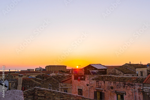 View of the rising sun above the rooftops against the pink sky. Red clay tiled roof in the old town of Palermo, Sicily, Italy