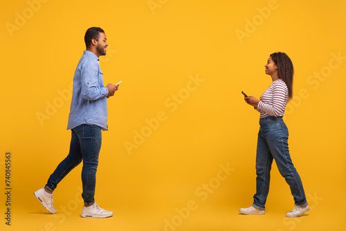 Black couple with mobile phones in hands walking past each other