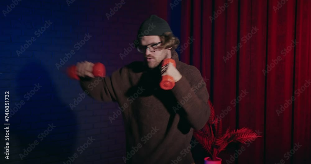 A young guy training his boxing skills using dumbbells on gradient background studio. Funny strong athlete practice his kickboxing moves. Thin sports man preparing for fight versus hooligans A young guy training his boxing skills using dumbbells on gradient background studio. Funny strong athlete practice his kickboxing moves. Thin sports man preparing for fight versus hooligans