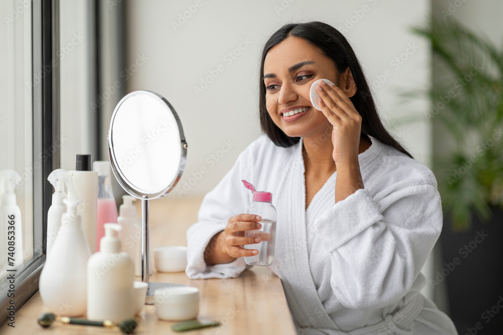 Positive young indian woman cleansing face in bathroom Positive young indian woman cleansing face in bathroom