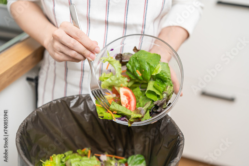 Compost from leftover food asian young housekeeper woman, female hand holding salad bowl use fork scraping waste, rotten vegetable throwing away into garbage, trash or bin. Environmentally responsible