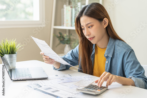 Stressed asian young employee, business woman calculate tax, income and expenses, hand holding bills of credit card for payment or payday on table at home office. Financial, finance people concept. photo