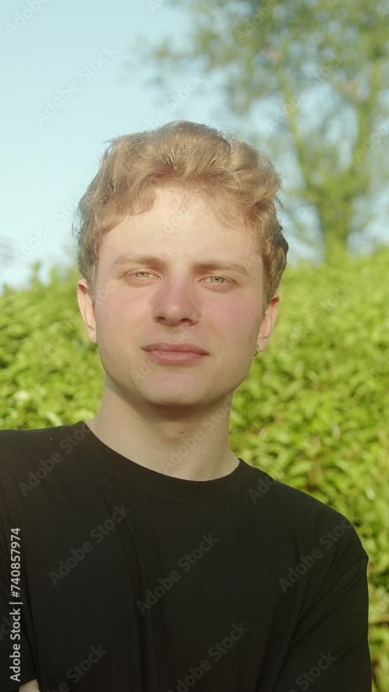 Vertical video. Radiant Smile: Portrait of Handsome Blond Young Male Model with Colored Eyes Gazing at the Camera Outdoors Vertical video. Radiant Smile: Portrait of Handsome Blond Young Male Model with Colored Eyes Gazing at the Camera Outdoors