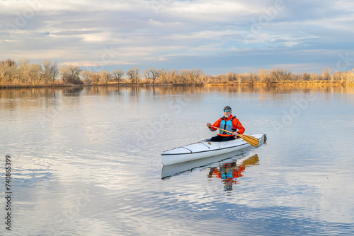 senior male paddler is paddling a decked expedition canoe on a calm lake in northern Colorado, winter scenery without snow