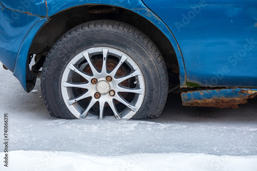 The rear wheel of an old blue car, frozen in ice. There is rust on the body. Close-up. Background.