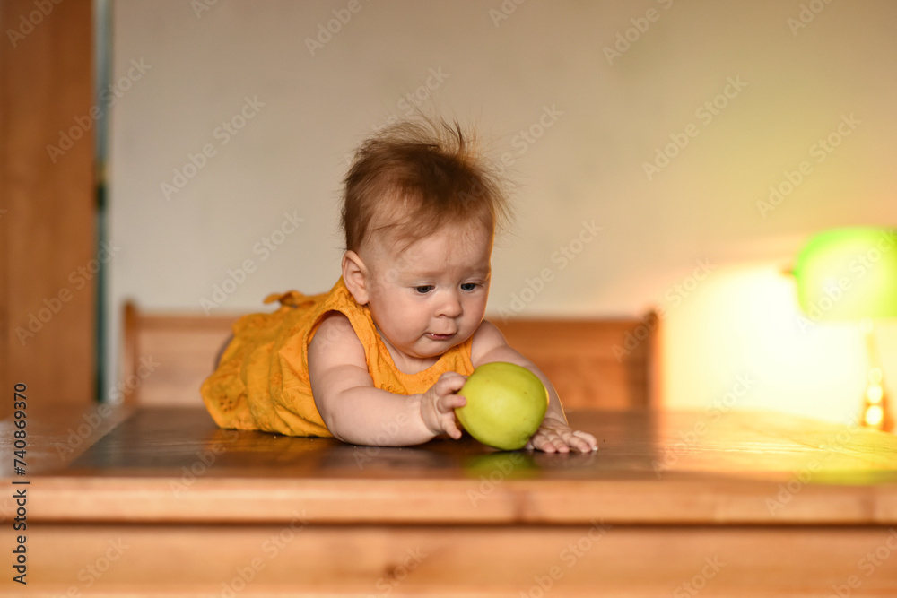 Fototapeta premium Small child with a green apple. The baby is lying on his stomach
