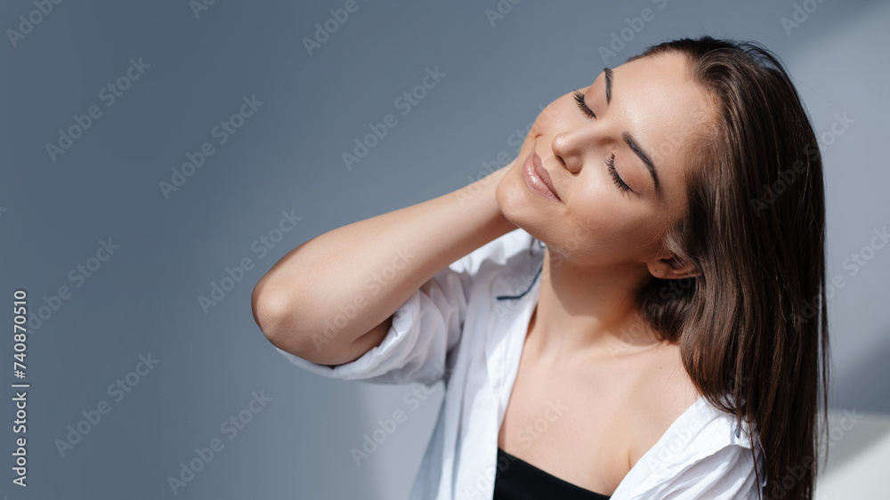 Smiling girl posing with closed eyes on grey background. Beautiful natural woman looking at copy space, spa and wellness concept Smiling girl posing with closed eyes on grey background. Beautiful natural woman looking at copy space, spa and wellness concept