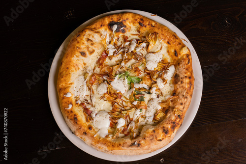 Pizza tradizionale napoletana con mozzarella, carciofi fritti, speck croccante, crema di formaggio e basilico fresco servita in una pizzeria photo