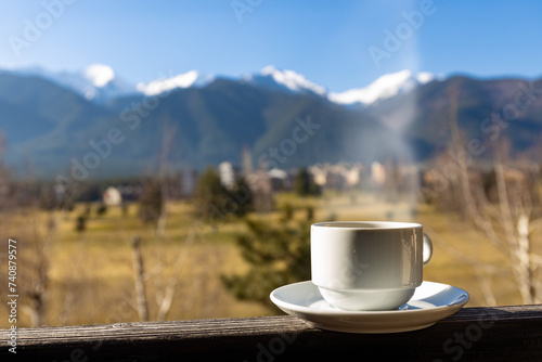 A cup of hot coffee on the background of a beautiful snowy mountain and a green field