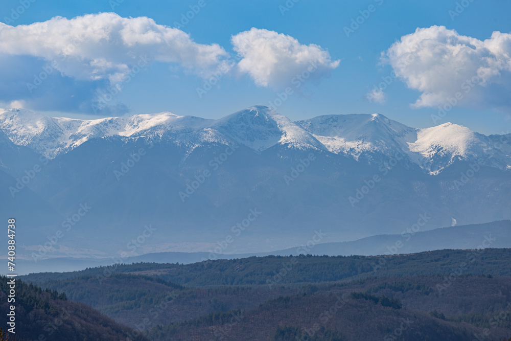 Snowy mountain peak, wooded valley and cloudy sky in February. Nature background, global warming, care for the planet.