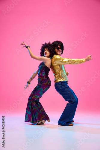 Konstfotografi Energetic disco dance lift, couple in 1970s fashion outfit dancing in motion with playful energy against gradient pink studio background