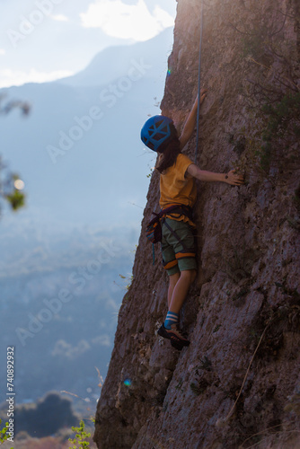 Children's rock climbing. A boy climbs a rock against the backdrop of mountains. Extreme hobby. Athletic child training to become strong.