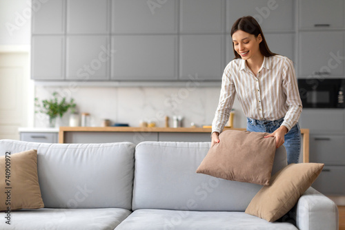 Smiling young woman arranging cushions on sofa