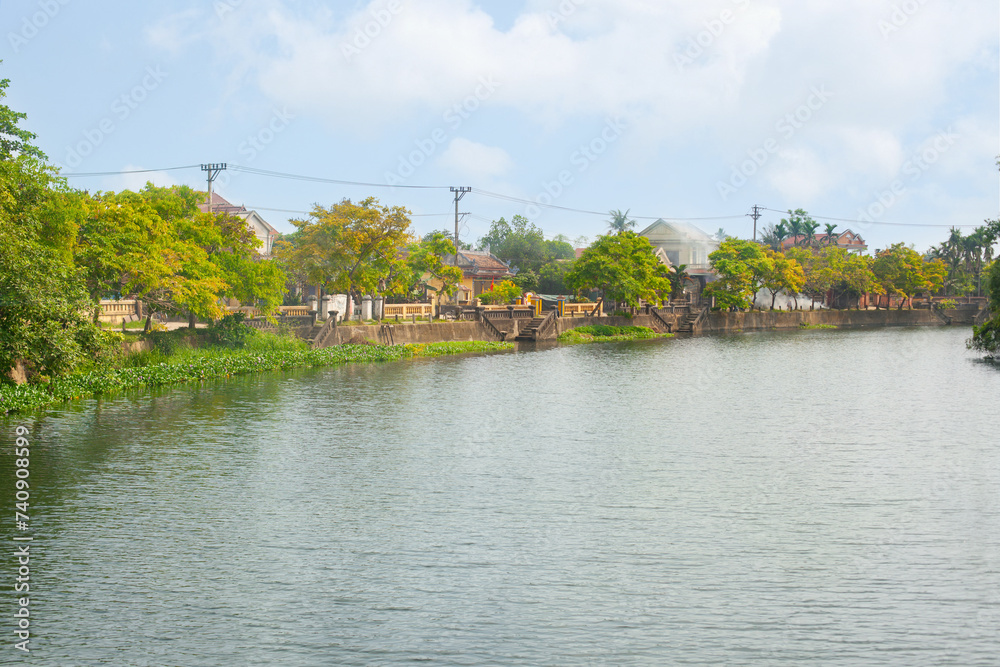 Fototapeta premium Serene riverside view with village and lush greenery on a sunny day in Hue city, Vietnam