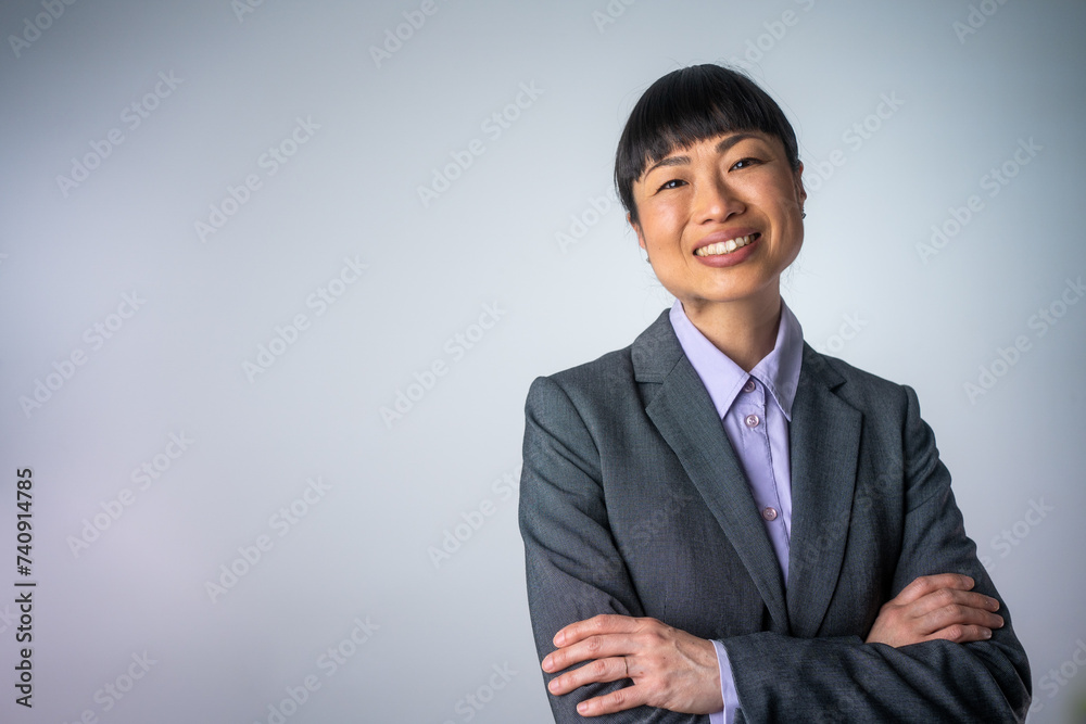 Cheerful Asian business woman in purple up shirt, smiling confident and cheerful with arms folded, isolated on a grey background. Isolated portrait of smiling business woman with crossed arms. Cheerful Asian business woman in purple up shirt, smiling confident and cheerful with arms folded, isolated on a grey background. Isolated portrait of smiling business woman with crossed arms.
