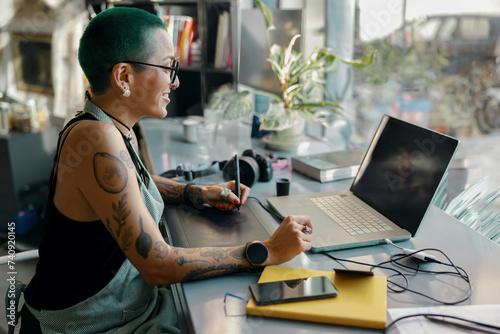 Woman designer uses graphics tablet and laptop for retouching photos or digital drawing in workshop