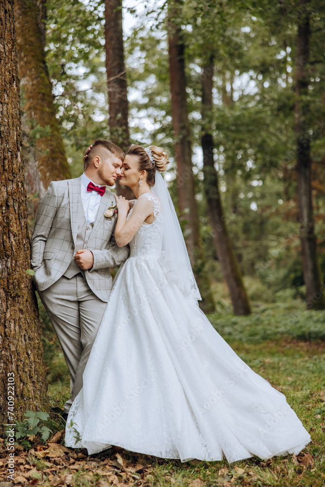 lovely and stylish newlyweds are hugging and smiling against the background of autumn nature in a beautiful garden. An incredibly beautiful young bride leaned against the shoulder of her beloved groom lovely and stylish newlyweds are hugging and smiling against the background of autumn nature in a beautiful garden. An incredibly beautiful young bride leaned against the shoulder of her beloved groom