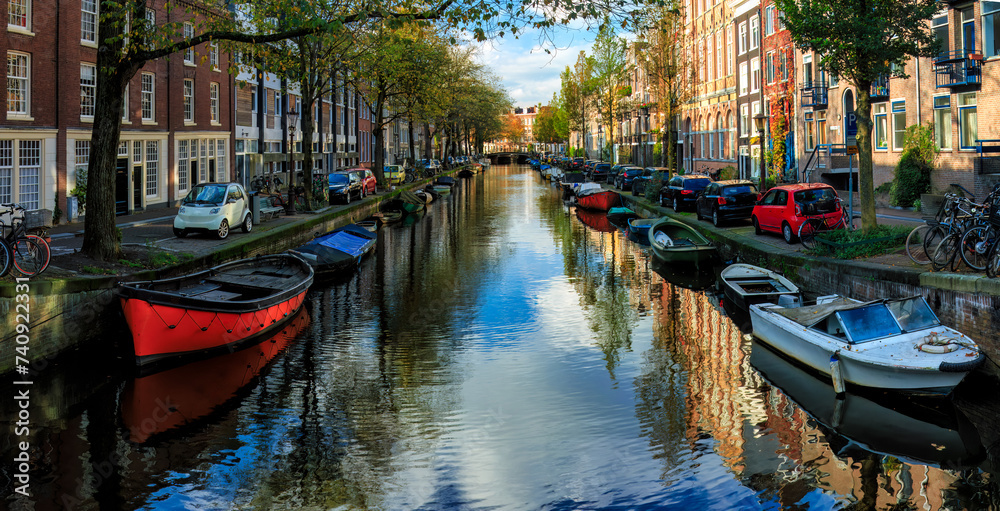 Panoramic view to famous  Amsterdam city center canal  with dutch brick buildings, trees , reflections  and  anchored boats in sunny autumn day. Nedherlands. 