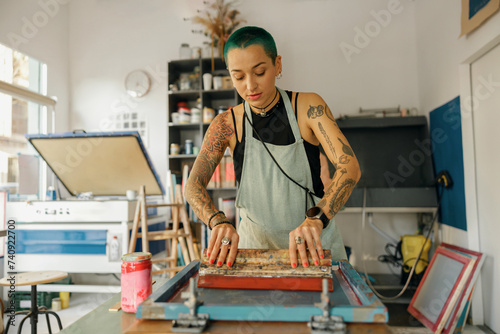 Female worker with squeegee is printing images on textile by silkscreen method in a design studio photo