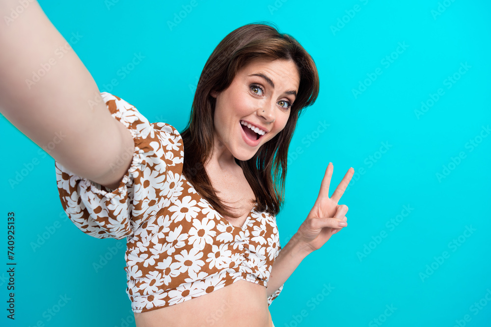 Fototapeta premium Self portrait of funny lady holding video camera recording content showing v sign shooting isolated on aquamarine color background