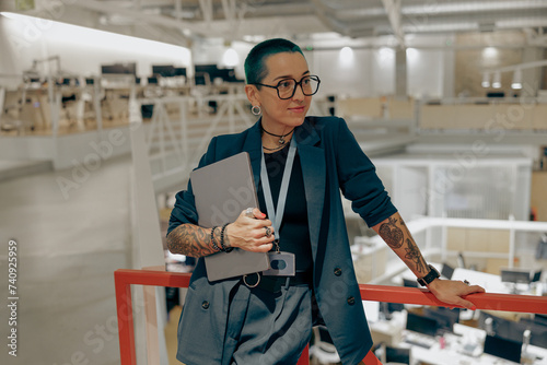 Fotografia Pretty tattooed female manager in glasses with laptop standing on modern coworki