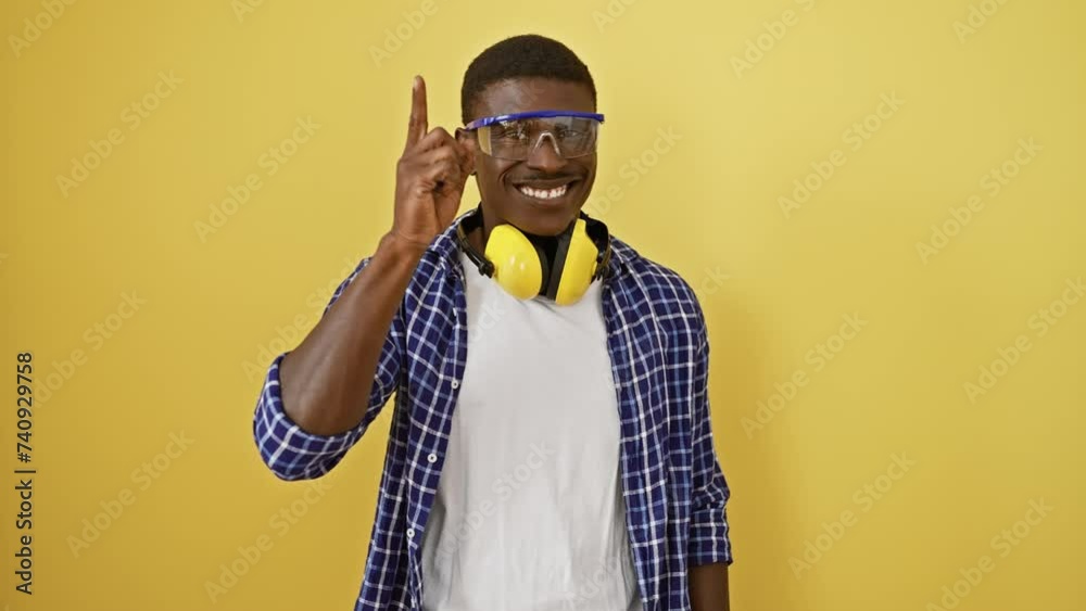 Giddy up! happy african american man in safety glasses scores the winning idea! pointing up for number one success on an isolated yellow background. Giddy up! happy african american man in safety glasses scores the winning idea! pointing up for number one success on an isolated yellow background.
