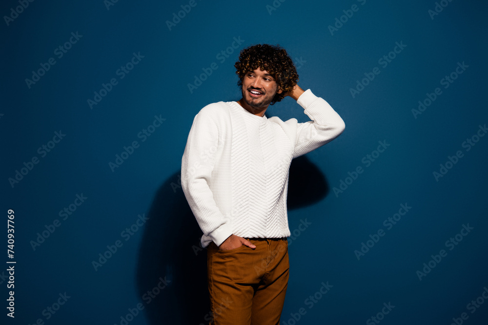 Portrait of curly hair young indian guy seems shy at first date looking empty space cheerful isolated on dark blue color background