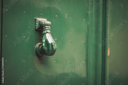 Old door knocker of historical building clode up. Doorknob in a shape of woman hand, on a green door. Italian exterior details. 