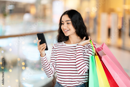 Happy young indian lady shopping at mall, using phone