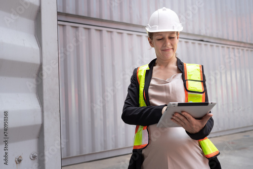 Logistic worker engineer pregnant woman use tablet computer working and checking with container at container site 