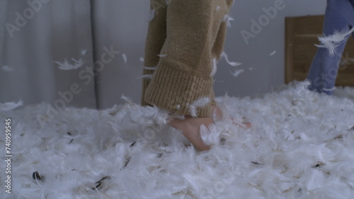 Child bouncing up and down in bed in slow motion with many feathers flying in the air in the midst of pillow fight  kids jumping up and down