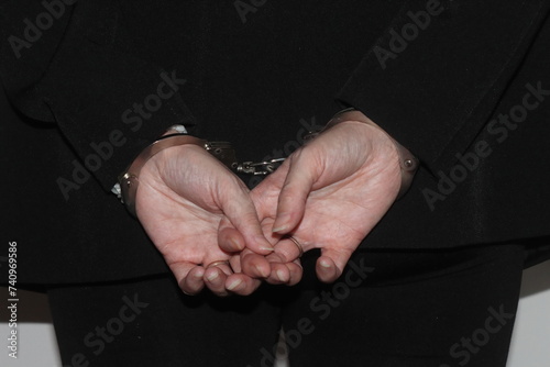 A close up of a woman's hands in handcuffs after she has been arrested. The woman is waiting to be transported to prison by the police.