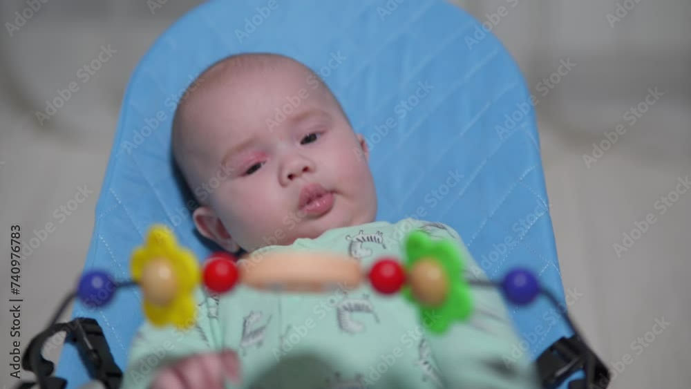 Newborn baby swings in a chaise longue and looks at hanging toys Newborn baby swings in a chaise longue and looks at hanging toys