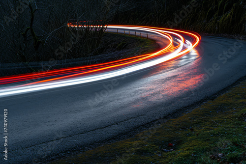 Traces from car headlights adorn the winding bend, painting a luminous path that gracefully curves through the road, adding an enchanting allure to the nocturnal journey through the scenic route. © Evgeniia